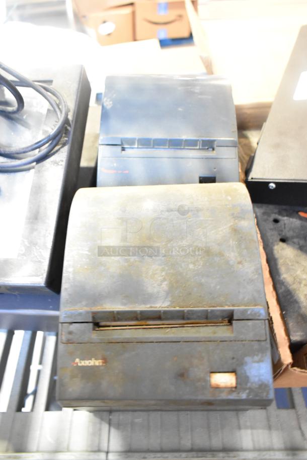 10 various items including used POS monitor, receipt printers, and wires. Printers show wear. “Axiohm” label visible.