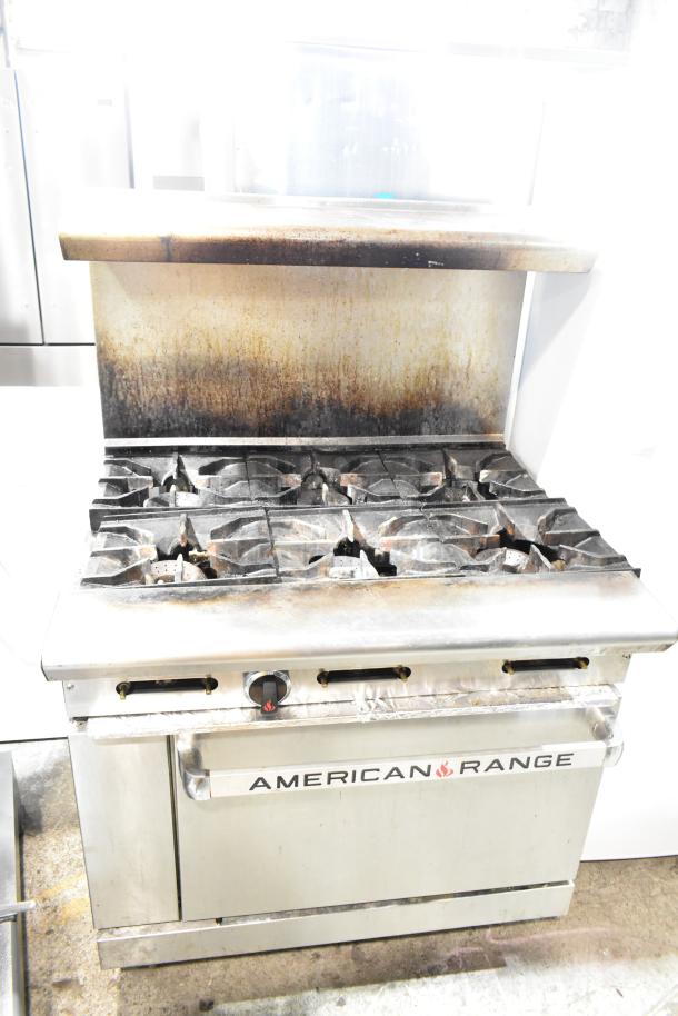 American Range commercial gas 6-burner range with oven, overshelf, backsplash. Visible wear, suitable for restaurant use.