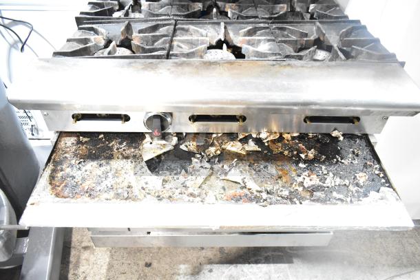 American Range commercial gas 6-burner stove with oven, over shelf, and backsplash. Shows signs of heavy use.