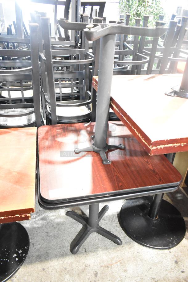 Two dining height tables with black tabletops and sturdy metal bases. Visible wear on edges, good for restaurant or cafe use.