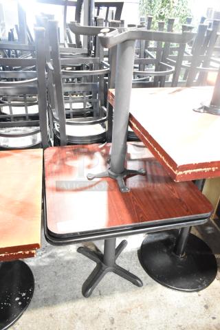 Two dining height tables with black tabletops and sturdy metal bases. Visible wear on edges, good for restaurant or cafe use.
