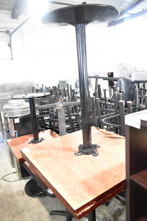 Two bar height tables with wood-patterned tabletops and sturdy metal bases, showing minor wear.