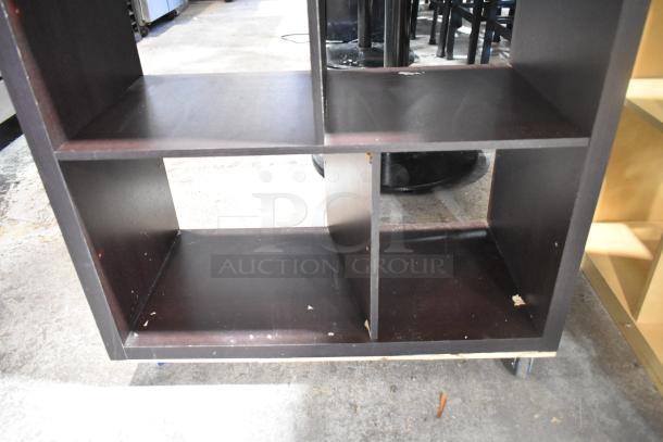 Dark wood bookshelf with a cube design, moderate wear, visible scuffs, and storage space, suitable for office or home use.