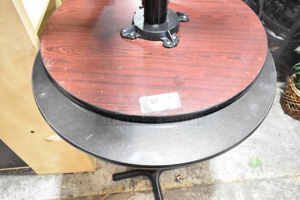 Two bar height tables with black tabletops and metal bases, minor surface marks. Auction tag marked "87 QTY."