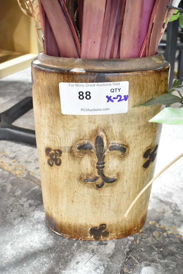 Antique-style planter with decorative fleur-de-lis pattern holding artificial maroon and green plants; auction tag indicates quantity x2.