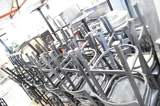 37 black metal bar height chairs with window back design and black seat cushions, stacked and in good condition.