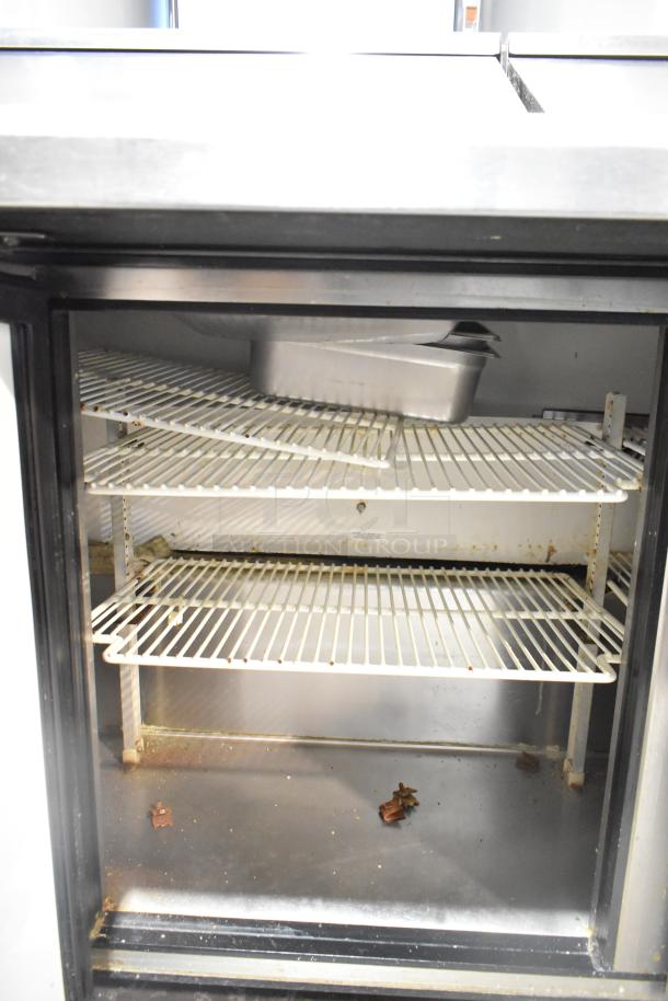 True TSSU-72-30M-B-ST sandwich prep table interior with wire shelves. Some rust and debris visible, indicates cleaning needed.