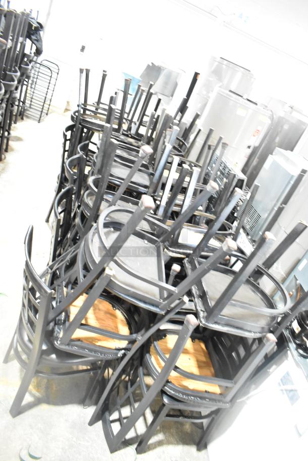 36 black dining height chairs with window back design and black seat cushions, stacked in storage.