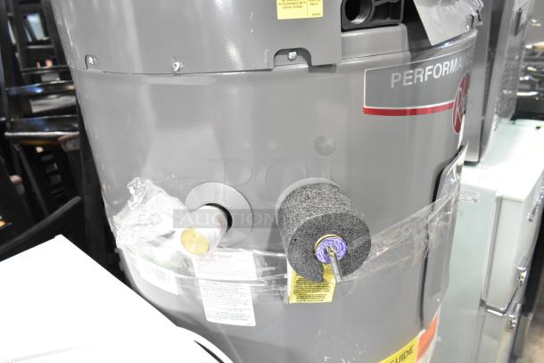 Rheem RSB565E Hot Water Heater, gray with protective wrapping. Features visible labels indicating model and safety instructions.