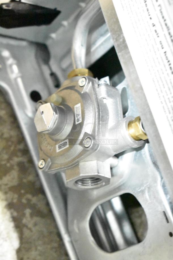 Frigidaire FCRG3052BSF gas range valve detail; silver metal with attached pipes and labeled markings.