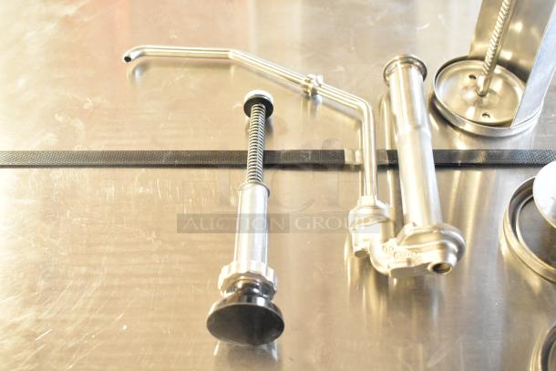 Stainless steel pump piece and caulk guns set on metal surface; includes valves and springs; clean, like-new condition.
