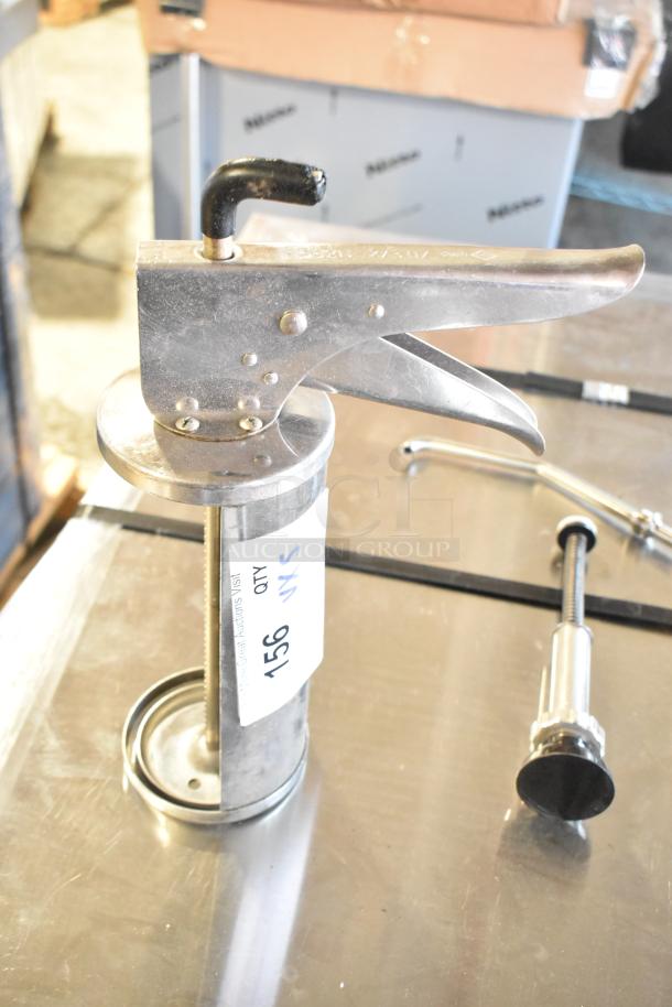 Metal pump piece and caulk guns on auction table, labeled "Qty 5, 156 VXS." Visible handle and metallic finish.