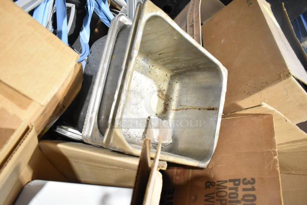 Assorted items including stainless steel drop-in bins and metal racks in used condition, scattered among cardboard boxes.