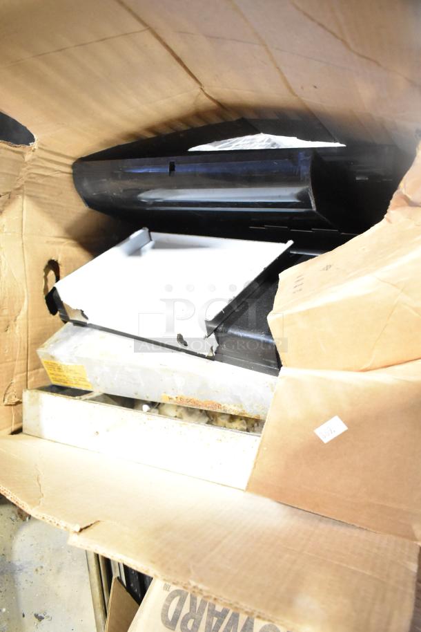 Assorted items in a cardboard box including stainless steel bins and metal racks. Slightly worn with visible label markings.