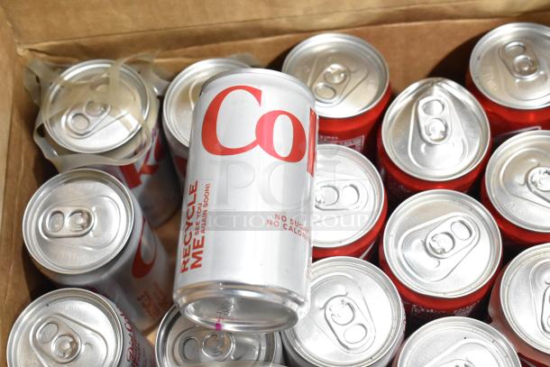 Box of assorted drink cans, featuring Coca Cola. Includes several cans, visible pull tabs, and branding details.