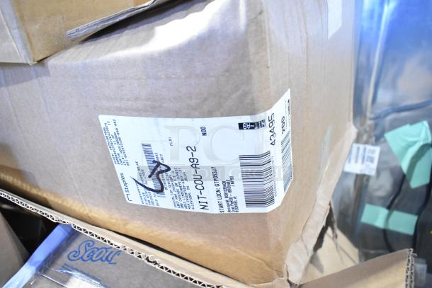 Cardboard boxes with labels indicating auction items including Pacific Blue 59589 Dispenser, Rubbermaid refills, and Diversey cleaner.