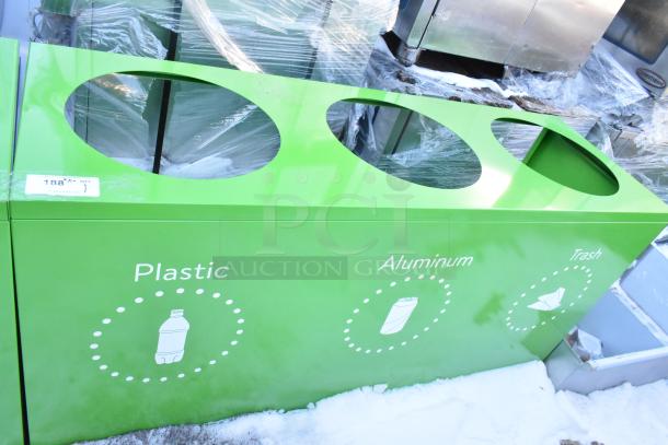 Brand new green recycling bin shell with three labeled deposit holes for plastic, aluminum, and trash. Visible scratch and dent.