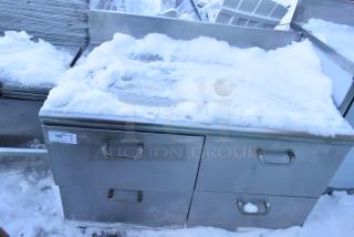Stainless steel work table with four drawers and backsplash, partially covered in snow, visible label "192".