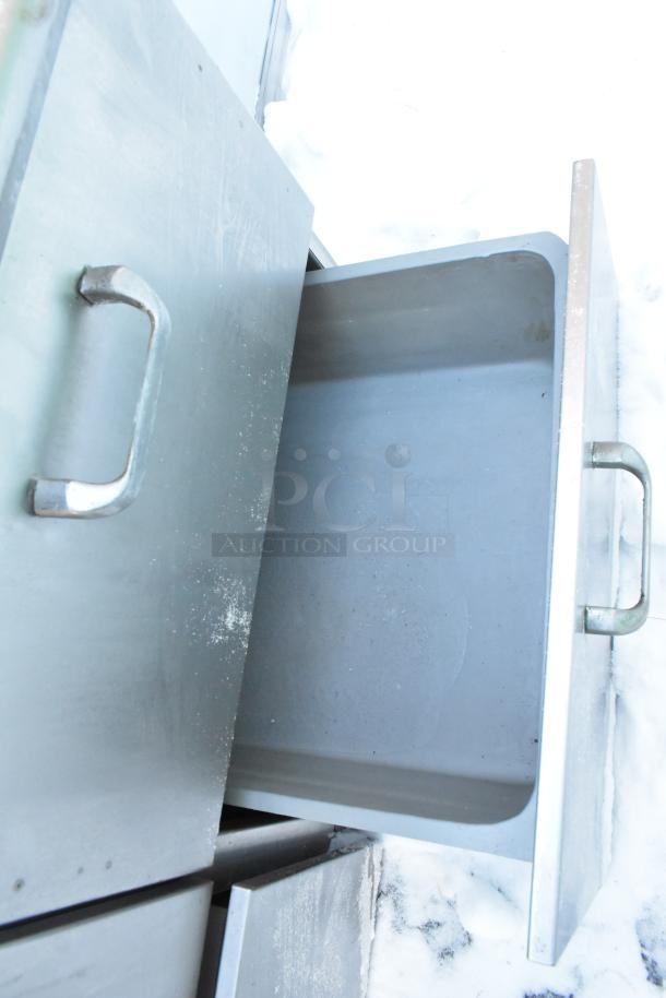 Metal work table with open drawer, stainless steel finish, visible handles, slight wear, includes four drawers and backsplash.