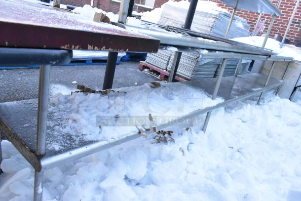 Four metal over shelves covered in snow, showing signs of wear, used for storage or display purposes.