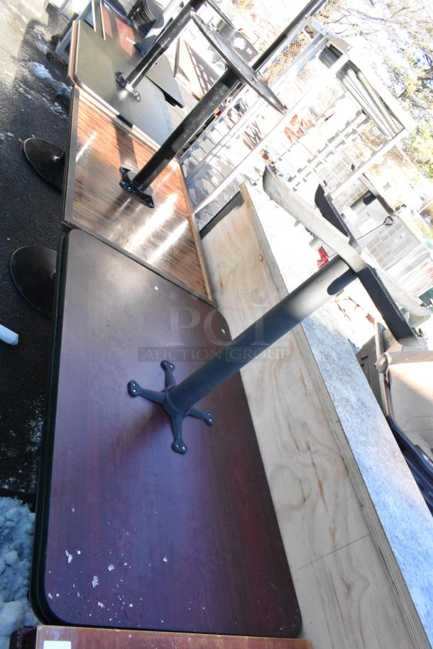 Eight various dining height tables with metal bases, used condition, mixed wood finishes, some surface wear visible.