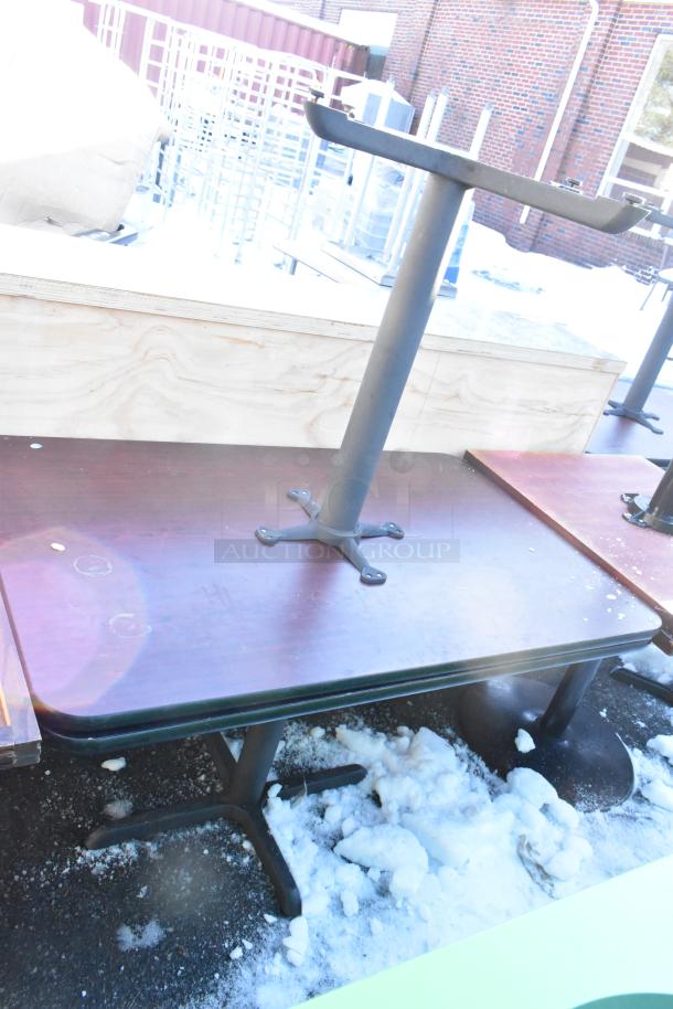 Eight dining height tables in a lot, featuring sturdy metal bases and wooden tops, showing wear and outdoor exposure.