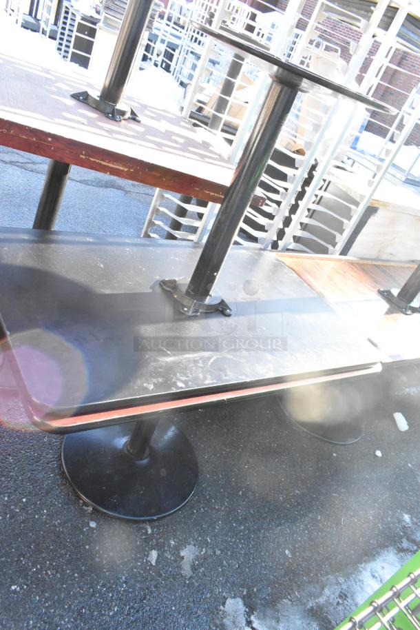 Eight various dining height tables with black tabletops and metal bases. Used condition with visible wear.
