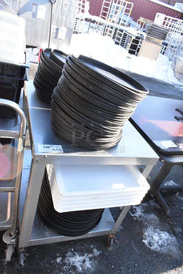 Stainless steel table with under shelf holding stacked metal round baking pans and white trays. Includes item tag “196” with quantity.