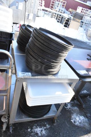 Stainless steel table with under shelf holding stacked metal round baking pans and white trays. Includes item tag “196” with quantity.