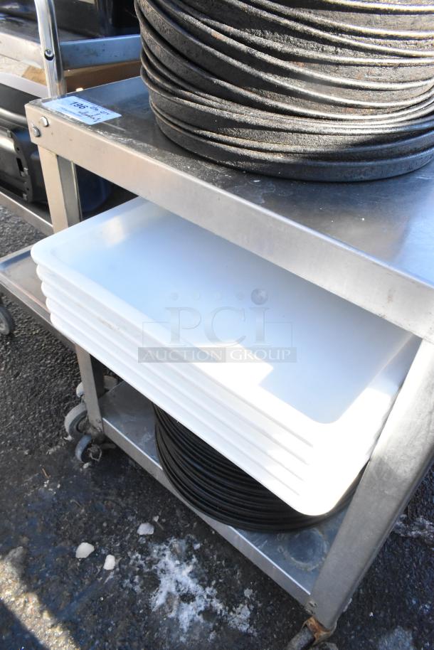 Stainless steel table with wheels, featuring an under-shelf. Includes stacked metal round baking pans and plastic trays. Item tag visible.