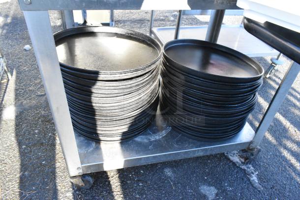 Stainless steel table with under shelf holding stacks of round metal baking pans, on casters.