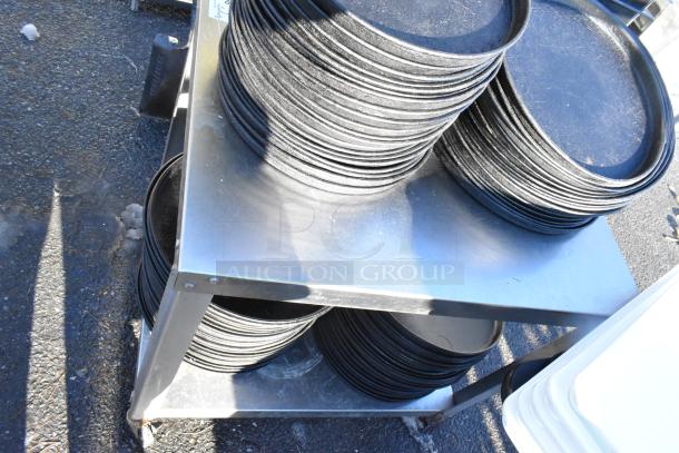 Stainless steel table with under shelf, holding stacks of round metal baking pans, used condition.