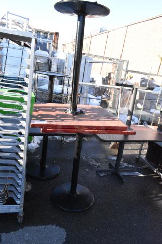 Two bar height tables with black metal bases and wooden tops, showing signs of wear. Ideal for commercial use.