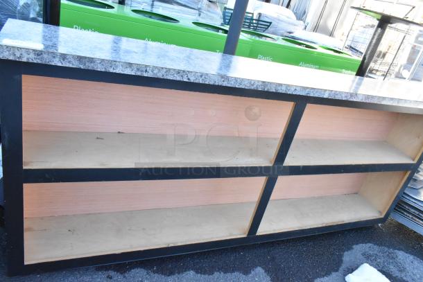 Wooden counter with black framing and granite-style top, featuring two open shelves. Good condition.