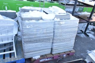 Stacks of 392 metal baking pans, full and half size, snow-covered, marked with lot numbers, ready for auction.