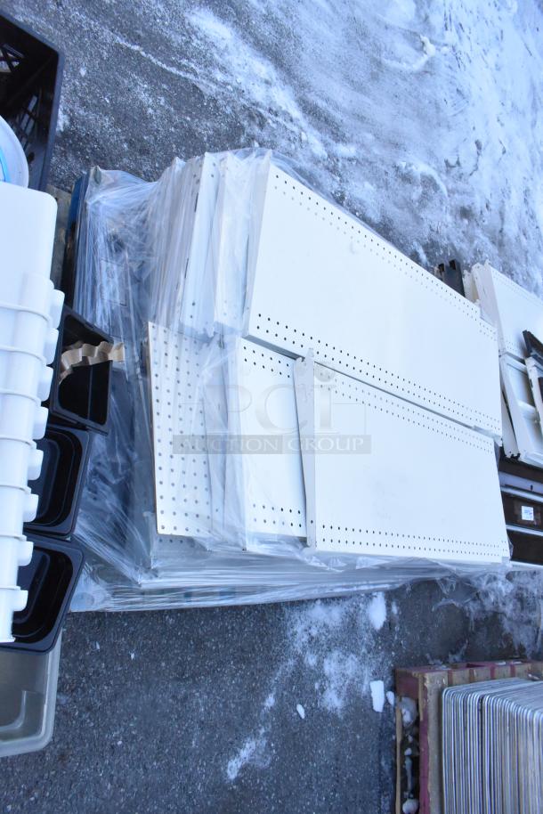Pallet lot of various items including white perforated shelves; bundled, wrapped, and stacked on a snowy outdoor surface.