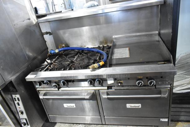 Garland commercial gas range with 6 burners, flat top, 2 ovens, over shelf, and backsplash, visible brand labels.