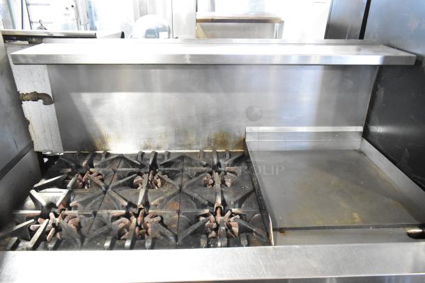 Garland commercial gas range with 6 burners, flat top, 2 ovens, shelf, and backsplash in used condition.