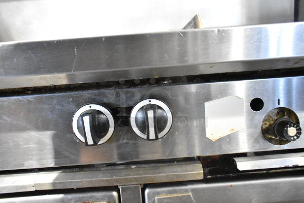 Garland commercial gas range with 6 burners, flat top, 2 ovens, overshelf, backsplash. Features control knobs, stainless steel finish.