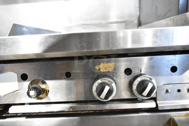 Garland commercial gas range, 6 burners, flat top, 2 ovens, over shelf, backsplash. Visible wear on knobs.