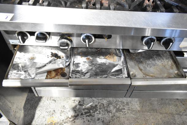 Garland commercial 6-burner gas range with flat top, two ovens, overshelf, and backsplash. Visible wear, foil-lined trays.