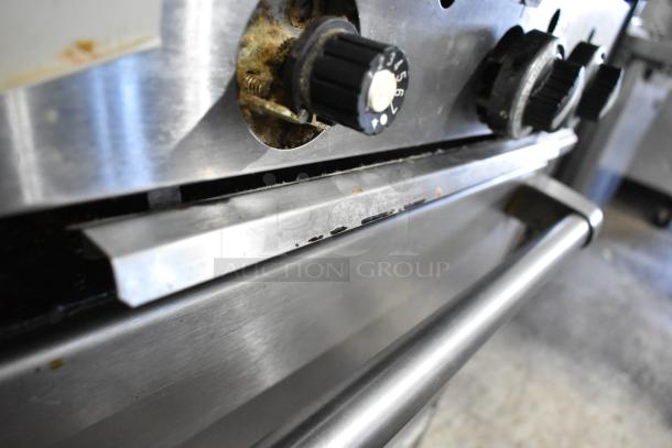 Garland commercial gas range, 6 burners, flat top, 2 ovens, used. Features knobs, shelf, and backsplash in stainless steel.