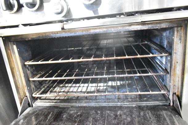 Garland commercial gas range with 6 burners, flat top, 2 ovens, overshelf, and backsplash. Some wear visible inside oven.