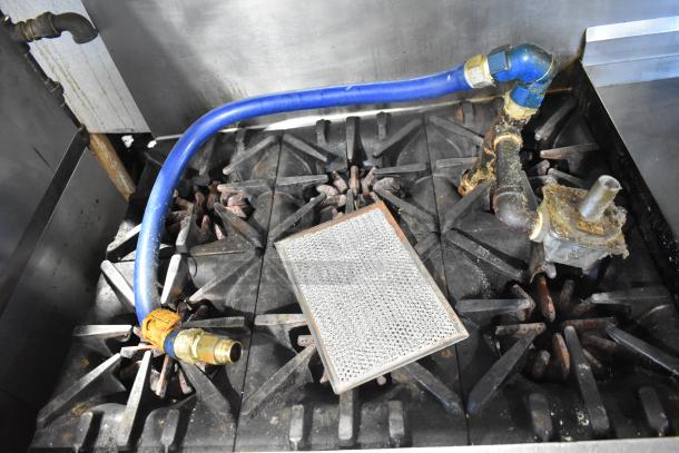 Garland commercial gas-powered 6-burner range top with visible gas hose and connection. Rust present on burners.