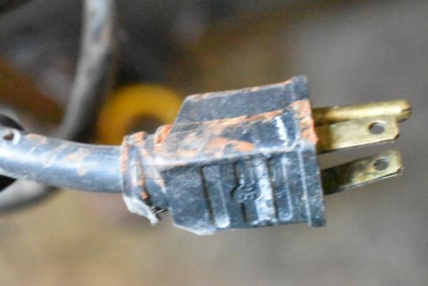 Close-up of a worn, black electrical plug with visible copper prongs, connected to a frayed cable.