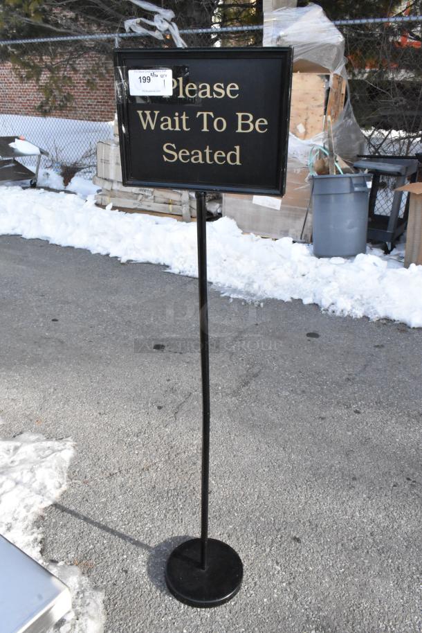 Freestanding metal sign reading "Please Wait To Be Seated" in gold text, black frame, price tag attached.