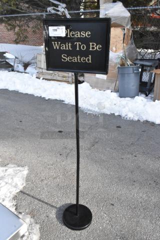 Freestanding metal sign reading "Please Wait To Be Seated" in gold text, black frame, price tag attached.