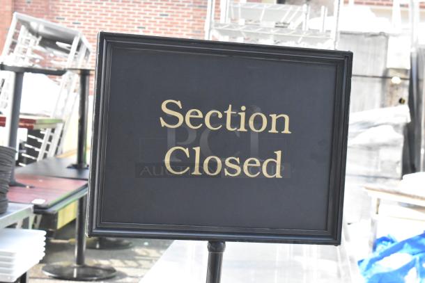 Black "Section Closed" sign with gold lettering, on a metal stand, used to indicate restricted areas.