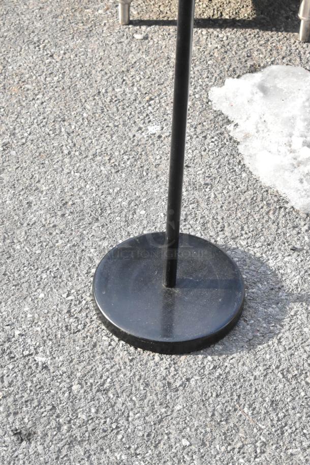Black metal sign stand on asphalt, featuring a round base.