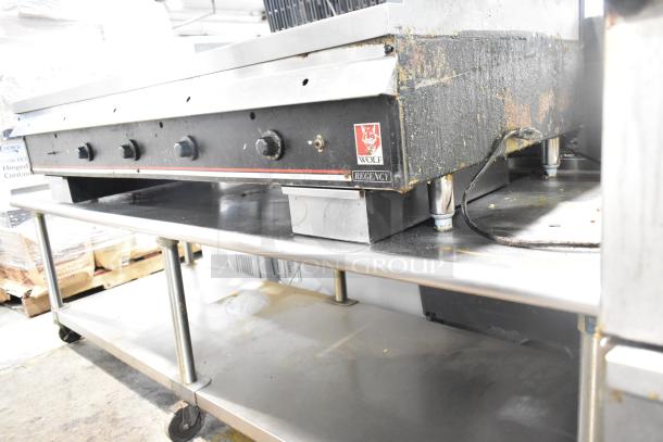 Wolf Regency commercial griddle with thermostatic controls on equipment stand, featuring commercial casters and visible wear.